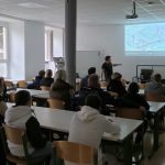 Profesor prikazuje teoretični pouk avtostroke pred učenci in starši v specializirani učilnici za avtostroko.