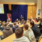 Dijaki v predavalnici poslušajo predstavitev predstavnika poklicne gasilske enote Celje, ki stojo spredaj.
