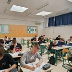 Dijaki sedijo v učilnici in rešujejo tekmovalne naloge. Zadaj na steni so plakati.