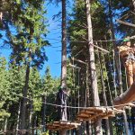 Dijaki stojijo v vrsti, so v naravi, oblečeni so v plezalna oblačila, saj gredo v adrenalinski park.
