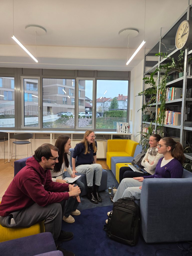 Skupina treh programerjev, dve ženski in en moški, predstavlja svojo idejo dijakinji s slepoto in mobilni učiteljici. Sedijo na modrih in rumenih foteljih v svetlem prostoru in se sproščeno pogovarjajo. V ozadju so police s knjigami in rastlinami.