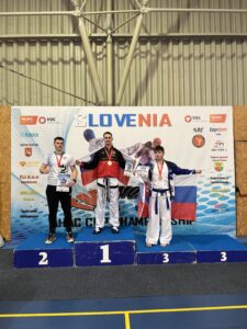 Naš dijak Nik Obrez je bil prvi na Taekwondo Ahac cup 2026. Stoji na stopničkah. Zraven še ostala tekmovalca.
